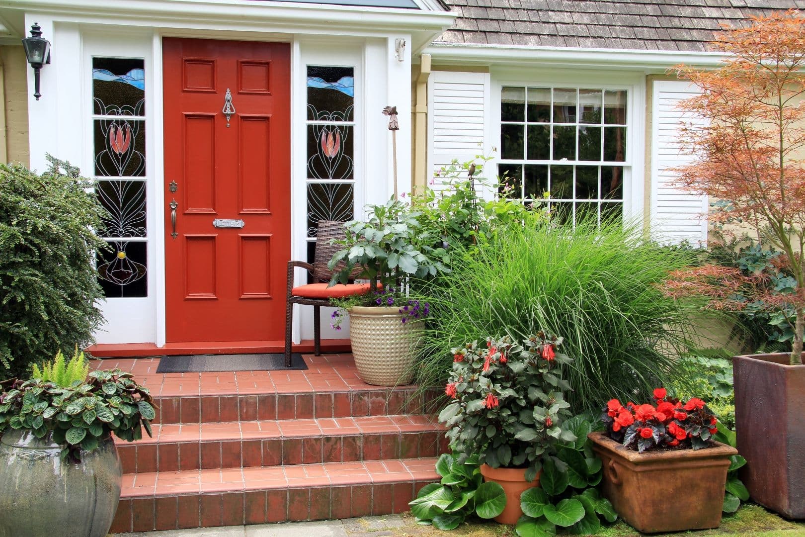 Charming small home with red front door and summer garden containers filled with annual flowers.