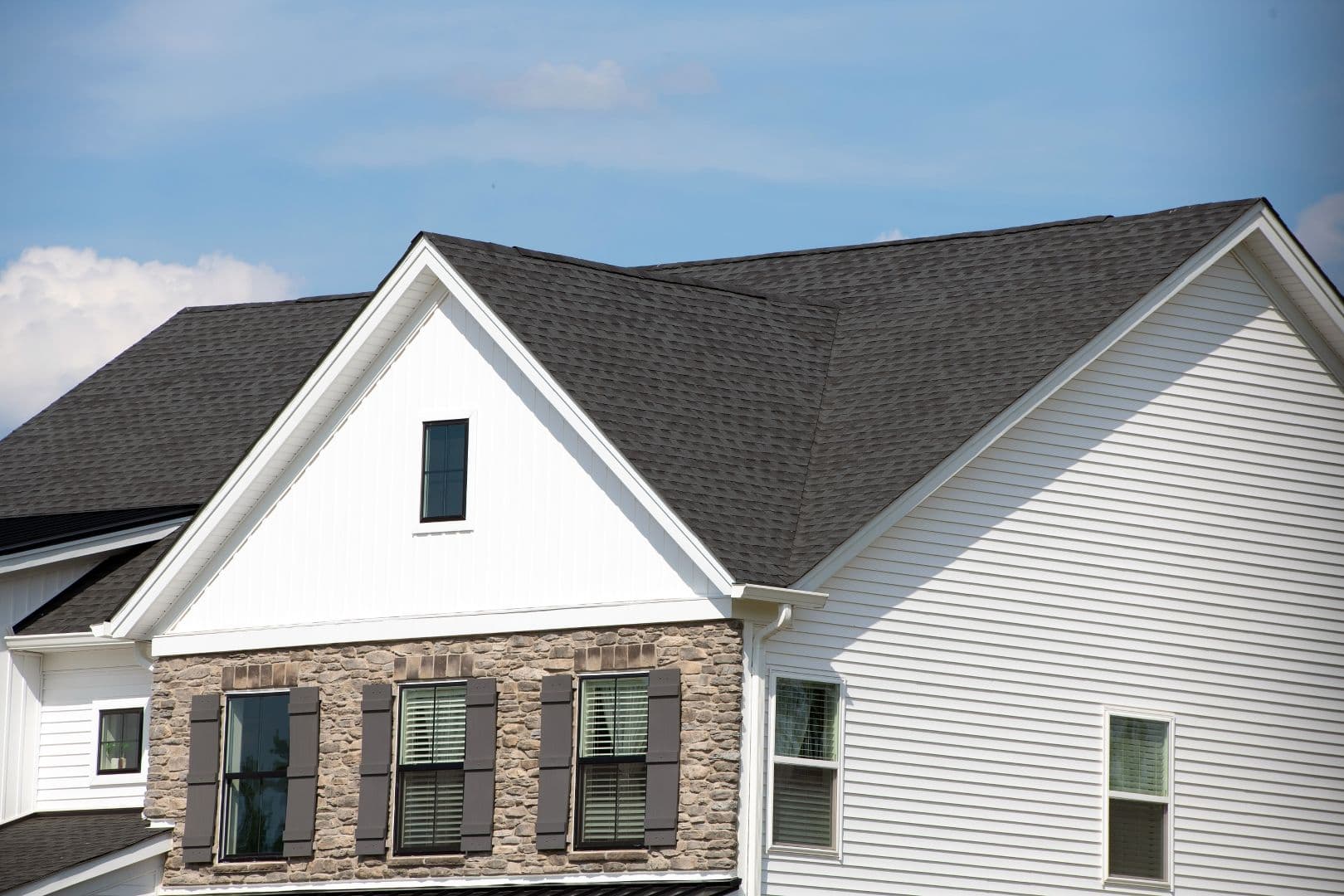 Edge Of Roof Shingles On Top Of a white and brick house.