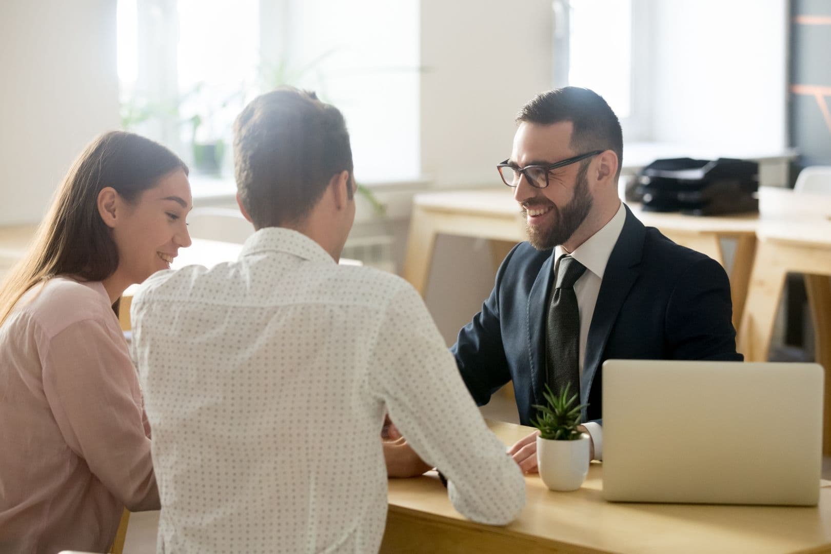 Three people in business attire meet at a desk.