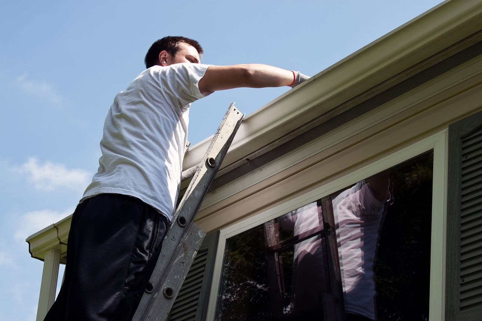 A person works on gutters on a ladder.