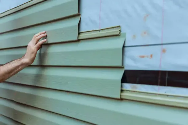 A contractor installs vinyl siding panels.