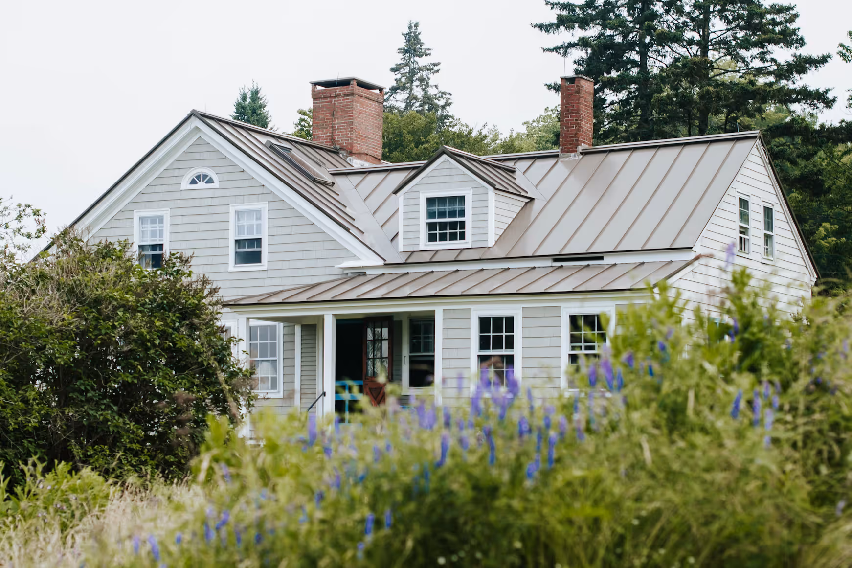 A light gray house with a light tan standing seam roof.