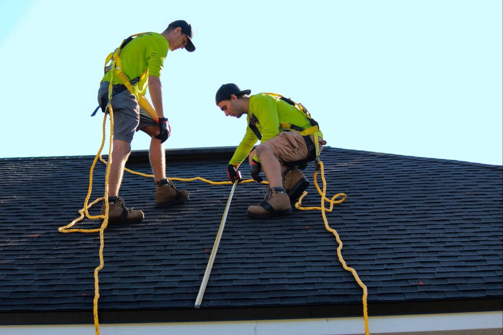 Two roofers take measurements on a roof.